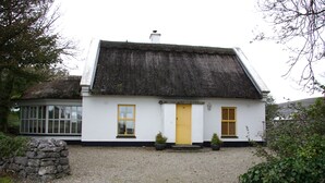 A white cottage with a thatched roof, a yellow door, and a stone wall to the left. - Ballyvaughan Cottage No 14 (Ballyvaughan)