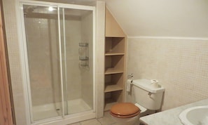 Un baño con cabina de ducha de vidrio, un inodoro con asiento marrón y pared con azulejos.