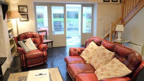 A living room with a red leather sofa, a leather armchair, and a small table with a lamp. There is a door leading to a garden. - Ballyvaughan Cottage No 2 (Ballyvaughan)