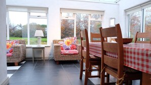 A sunlit room with a dining table and chairs, a wicker sofa, and a small table with a lamp. - Ballyvaughan Cottage No 2 (Ballyvaughan)