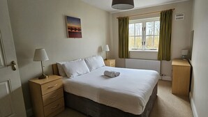 Quarto bem arrumado com uma cama, mesas de cabeceira, abajur, radiador e janela com cortinas.
