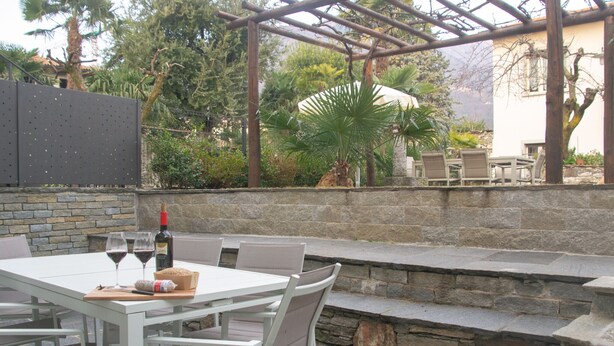 An outdoor patio with a white table and chairs, a stone wall, and a pergola. - Casa King - Welchome (Cannobio)