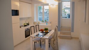 A modern kitchen with white cabinetry, a dining table with chairs, a built-in oven, and a window with a view of the outside. - Casa King - Welchome (Cannobio)