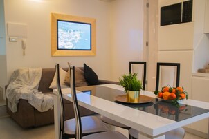 Ein modernes Wohnzimmer mit einer Couch, einem Couchtisch mit Topfpflanze und Obstschale sowie einem flachbildfernseher an der Wand.