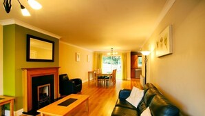 A living room with a fireplace, a black leather sofa, a wooden coffee table, and a dining area with chairs and a table. - Bunratty West No 40029 (Bunratty)