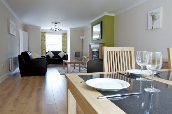 A modern living room with a dining area, featuring a sofa, a dining table set with plates and glasses, and a television.