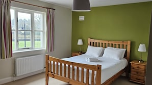 A bedroom with a wooden bed, two bedside tables, a window with curtains, and a green wall.