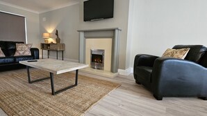 Una sala de estar con chimenea, un sofá, una mesa de centro y un televisor montado en la pared.