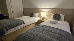 Habitación de hotel con dos camas, una mesita de noche con lámpara y una ventana con vistas.