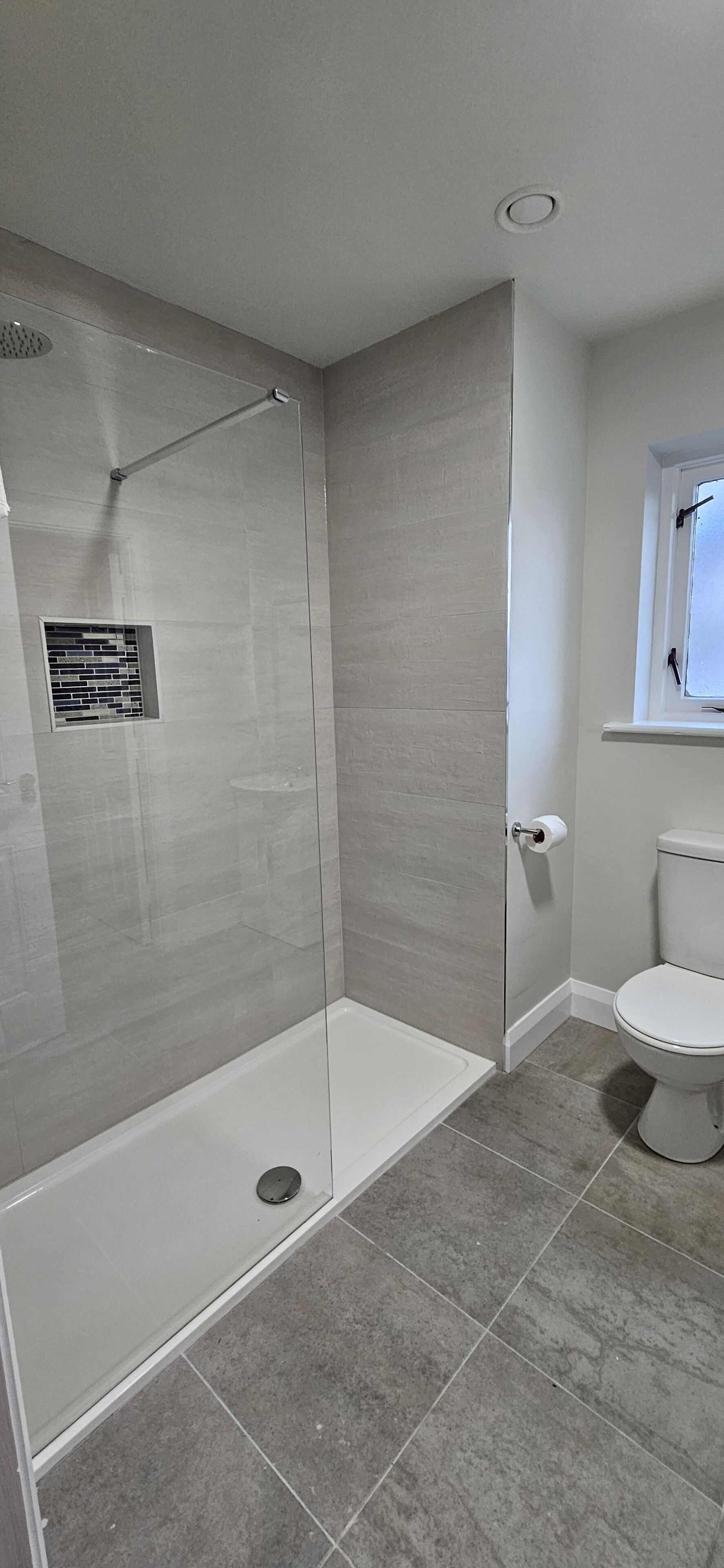 A modern bathroom with a shower, a toilet, and a window.