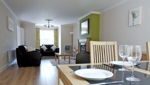 A modern living room with a dining area, featuring a sofa, a dining table set with plates and glasses, and a television. - Bunratty West No 40026 (Bunratty)