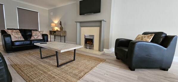 A living room with a fireplace, a sofa, a coffee table, and a TV mounted on the wall. - Bunratty Town House No 2 (Bunratty)