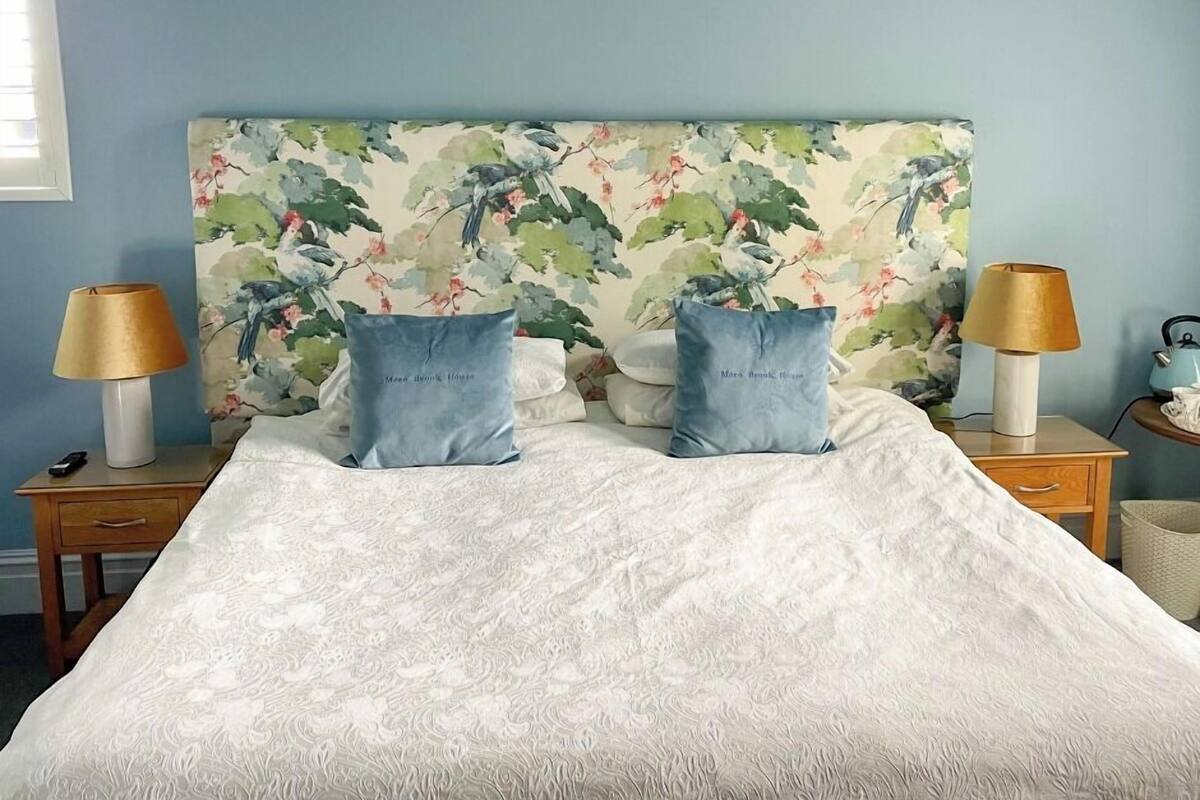 A bedroom with a floral headboard, two pillows, a white bedspread, and two bedside lamps.