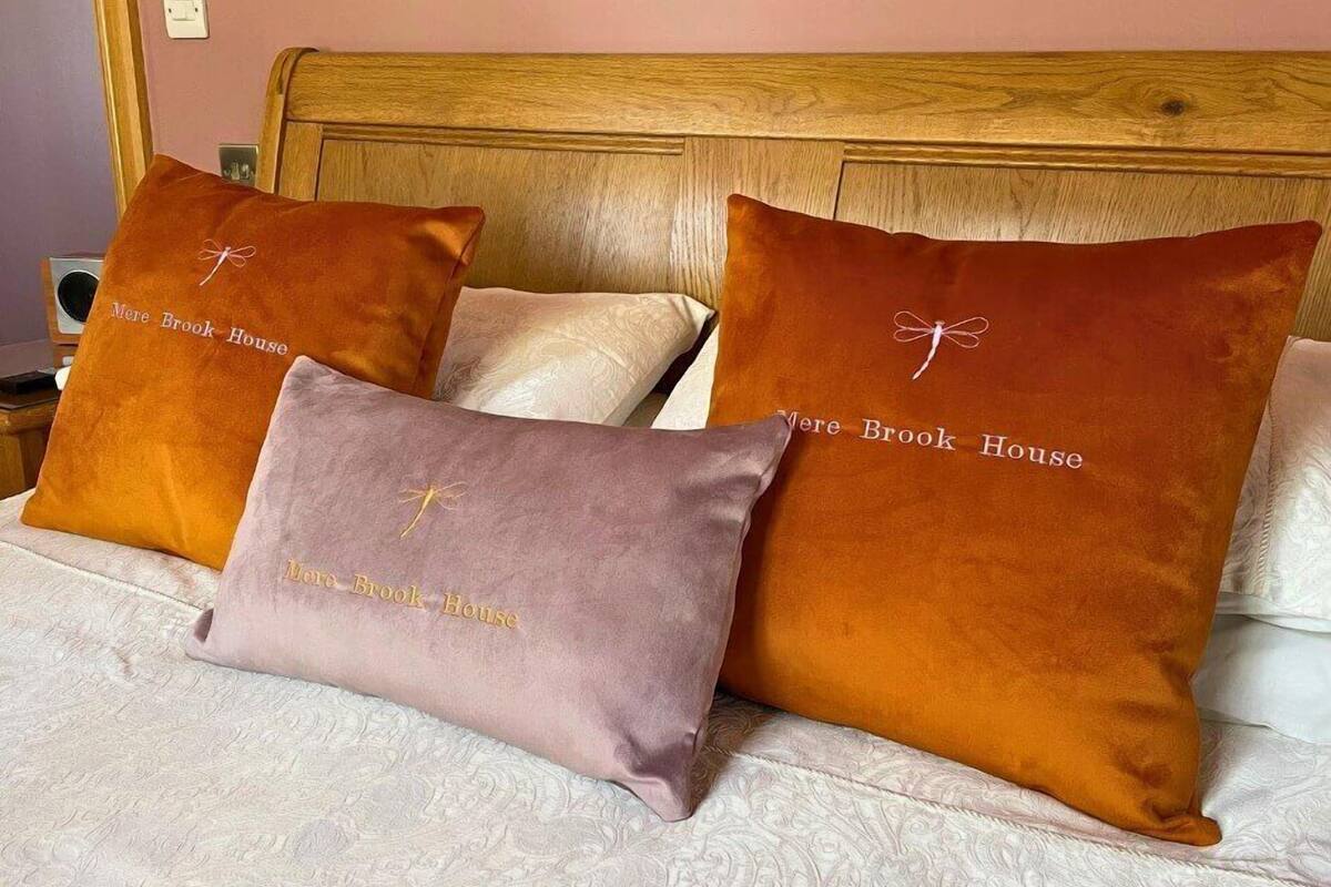 A bed with three pillows, two of which have 'More Brook House' embroidered on them.