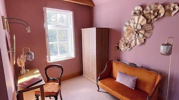 Une pièce avec un plafond en pente, un bureau en bois avec une chaise, un canapé, une armoire et une décoration florale fixée au mur.