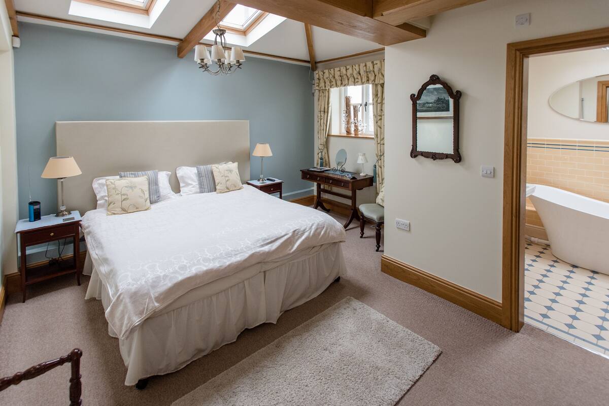 A bedroom with a large bed, bedside tables, a desk, a mirror, and a skylight.