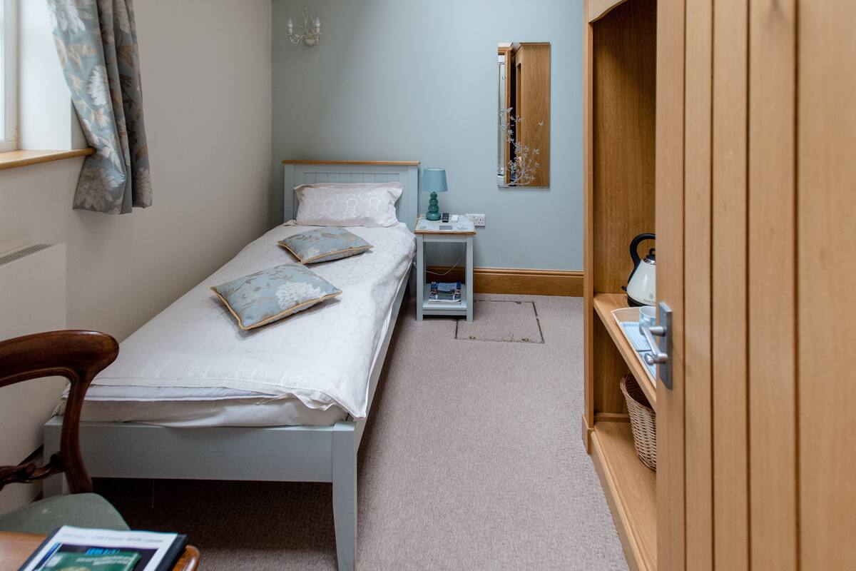 A small bedroom with a single bed, a nightstand, a chair, and a wooden wardrobe.