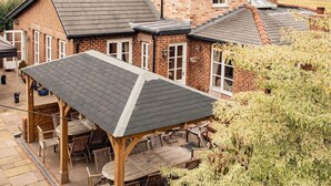 A large brick house with multiple gabled roofs and a covered patio area with outdoor furniture. - Mere Brook House (Wirral)