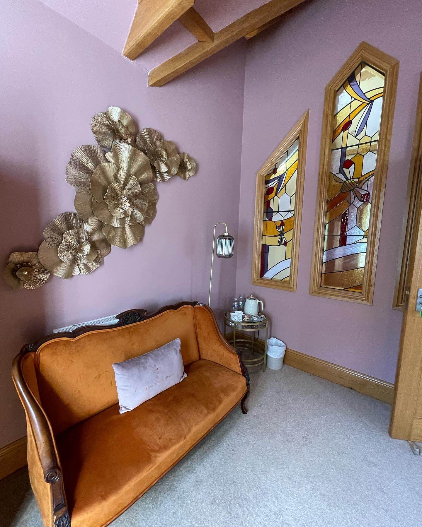 A room with a vintage orange sofa, a decorative wall piece, and two stained glass windows.