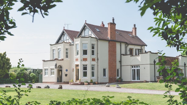 A large, two-story house with a symmetrical facade, multiple chimneys, and a well-maintained lawn. - Mere Brook House (Wirral)