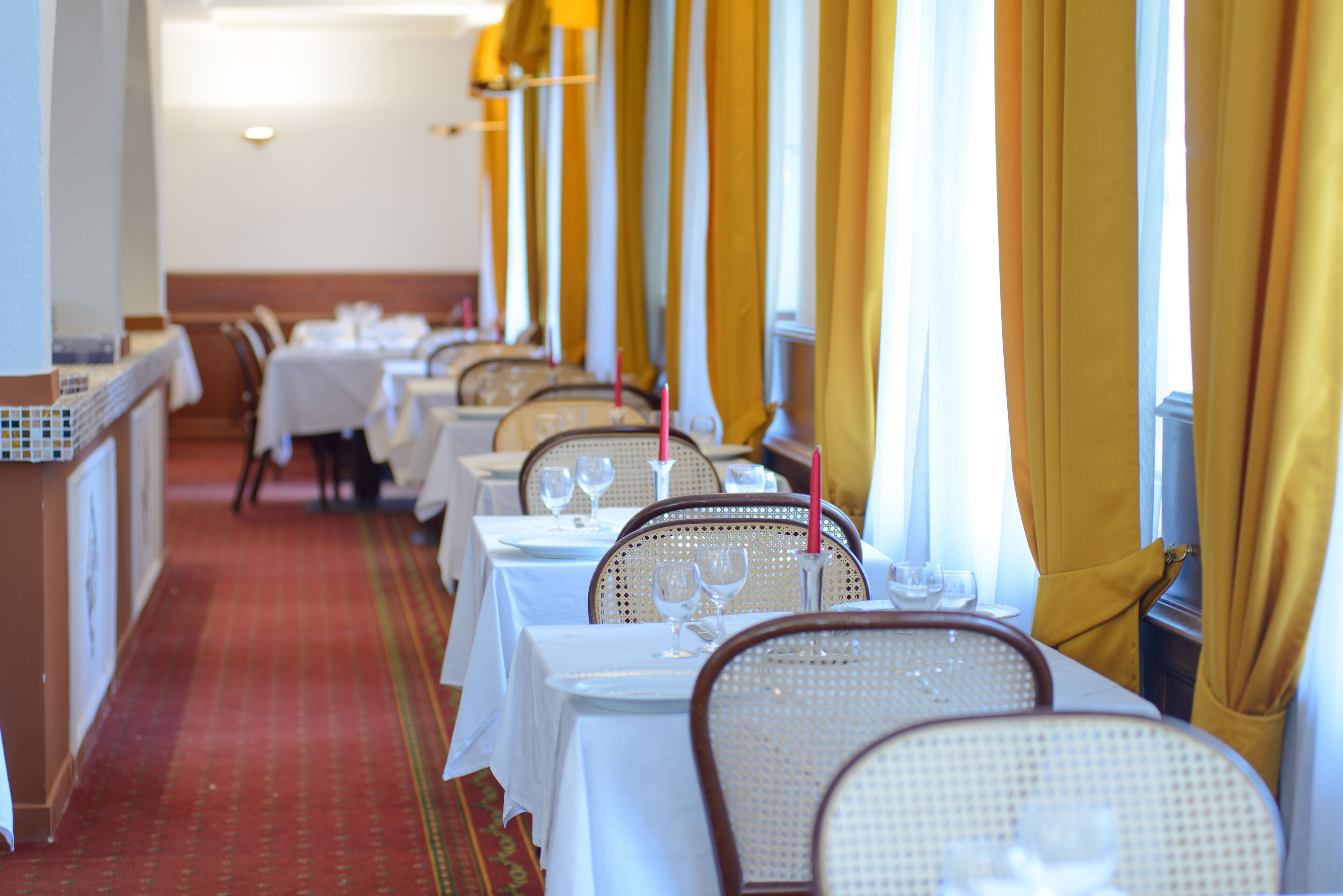 A restaurant with tables set for dining, featuring white tablecloths and wicker chairs.