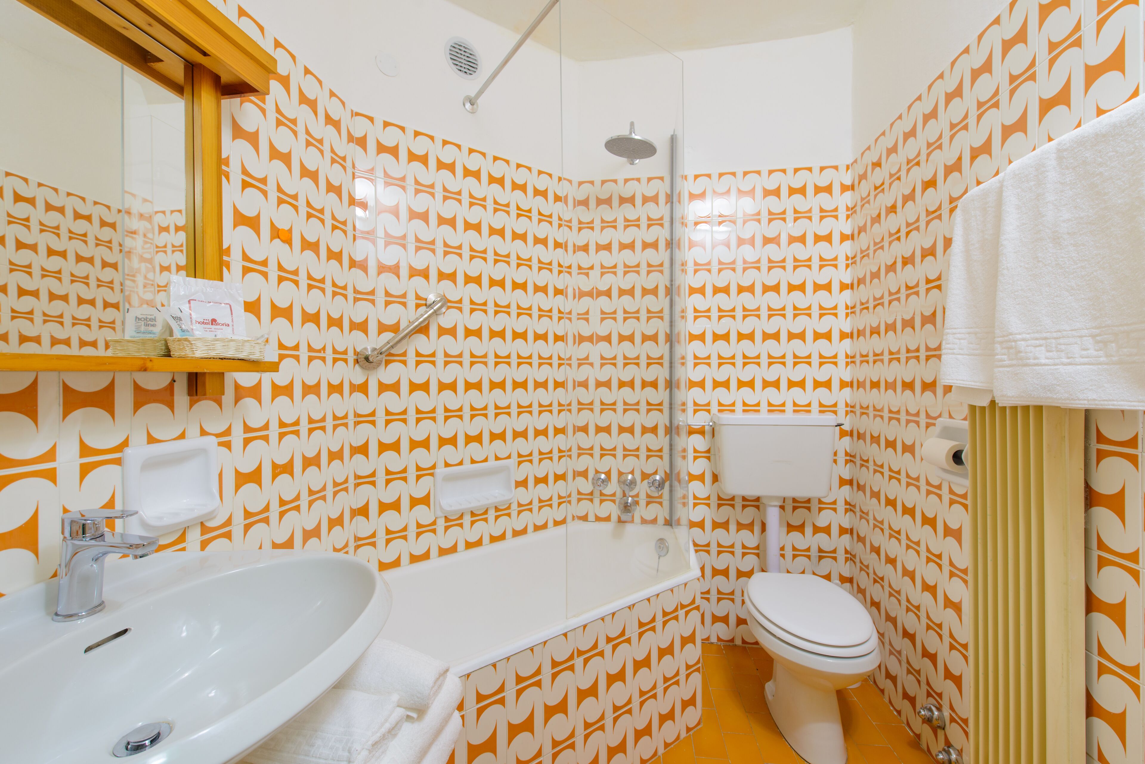Un baño con un lavamanos blanco, una bañera y un inodoro. Las paredes tienen un papel tapiz estampado.