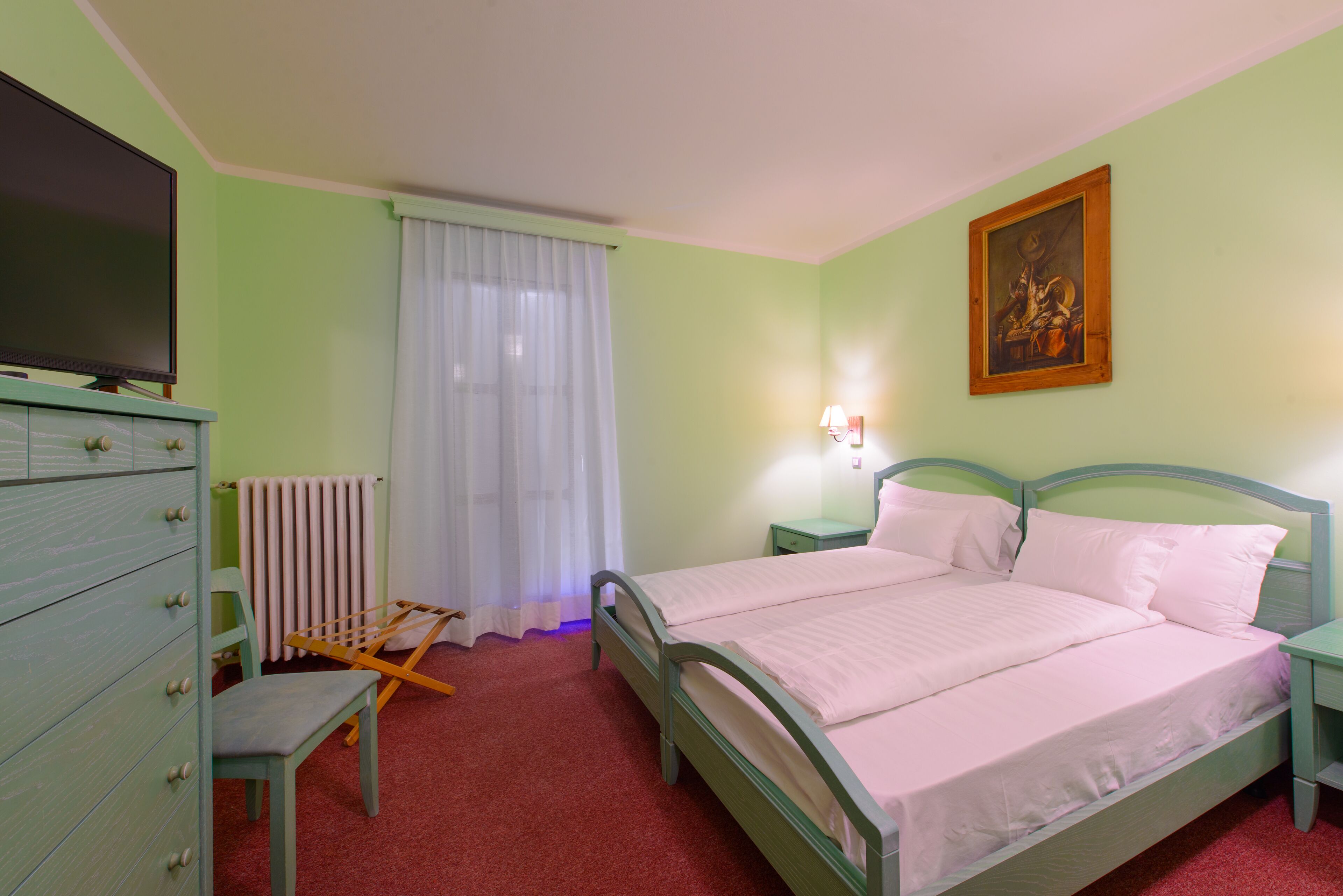 A bedroom with a bed, a dresser, a chair, a radiator, a television, and a painting on the wall.