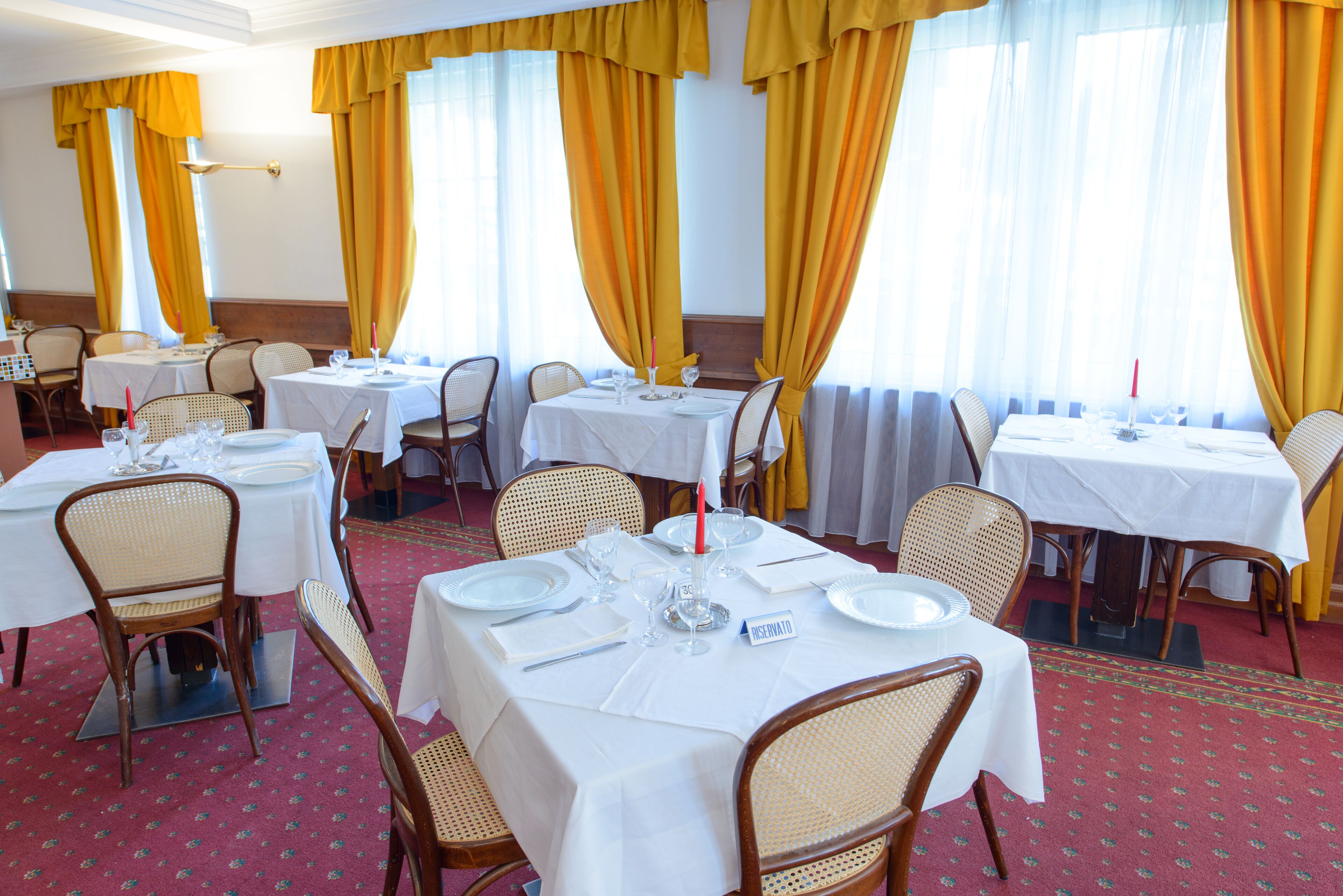 Un espace repas avec plusieurs tables dressées pour les convives, agrémenté de nappes blanches et de chaises en osier.