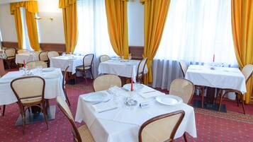 Un espace repas avec plusieurs tables dressées pour les convives, agrémenté de nappes blanches et de chaises en osier.