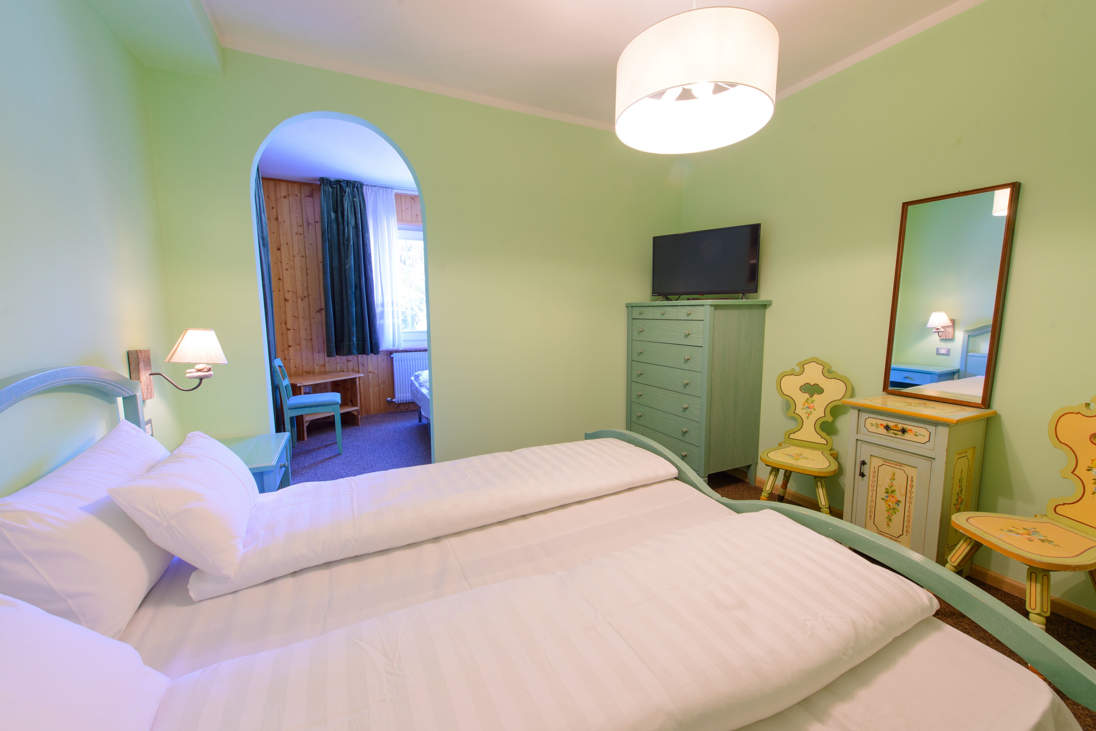 A room with a bed, a desk, a dresser, a television, and a mirror.