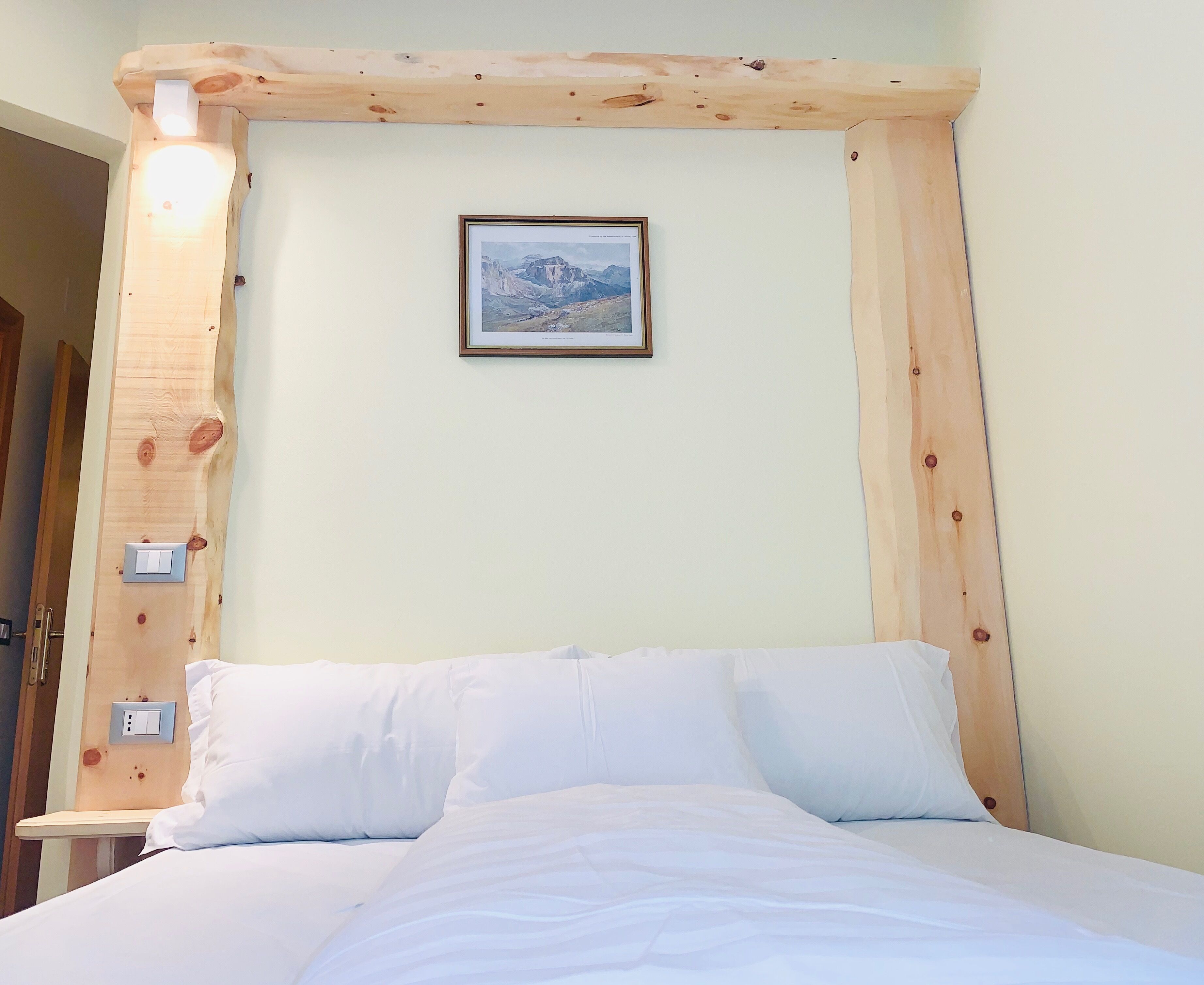 A bedroom with a wooden headboard, a framed picture on the wall, and a bed with white bedding.
