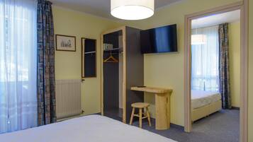 Un dormitorio con cama, escritorio, silla, perchero y televisor.
