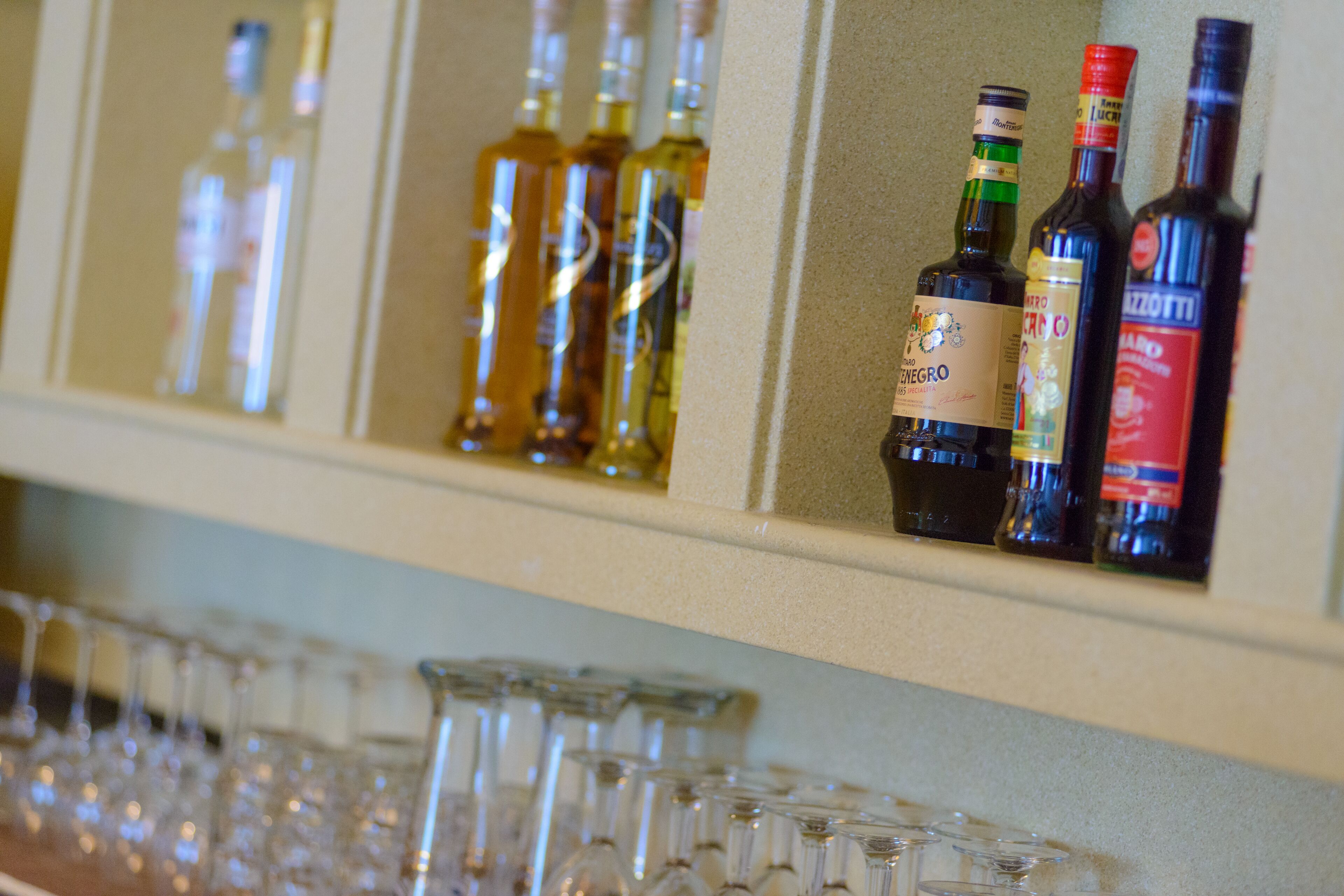 A bar area with shelves of liquor bottles and a row of empty glasses.
