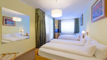 A hotel room with two single beds, a large mirror, a wooden chair, and a window with curtains.