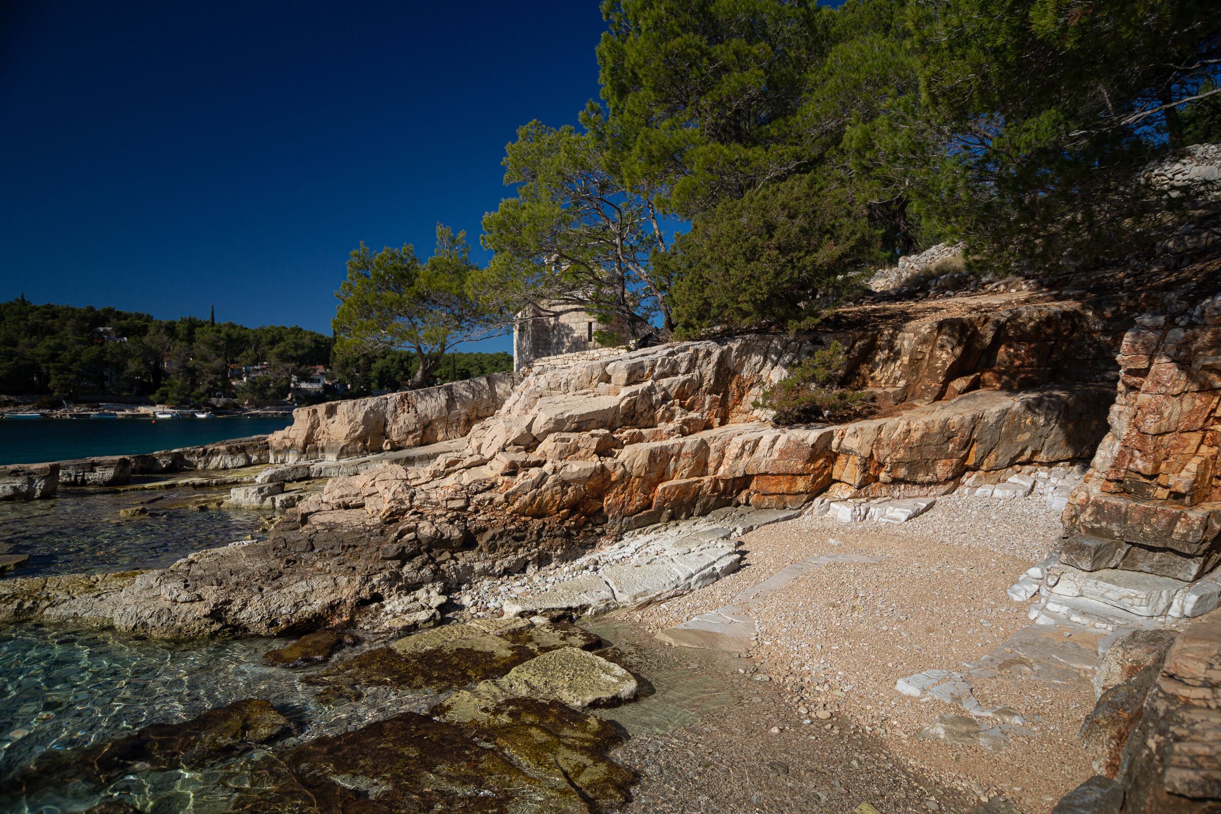 A rocky coastal area with clear water, a stone structure, and dense trees.