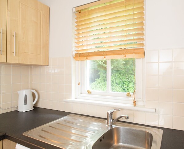 A kitchen with a stainless steel sink, a kettle, and wooden cabinets. - Castle Gardens 3 bed 4018 (Bunratty)
