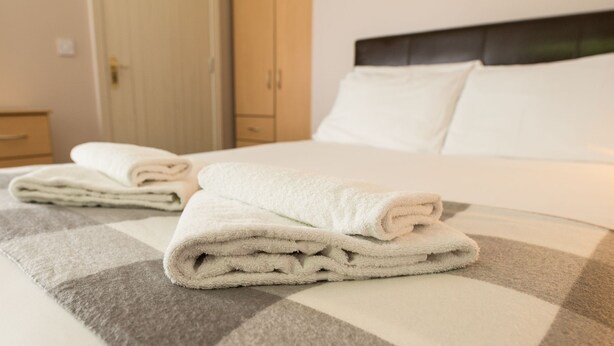 Een net opgemaakt bed met een geruit plaid en opgevouwen handdoeken.