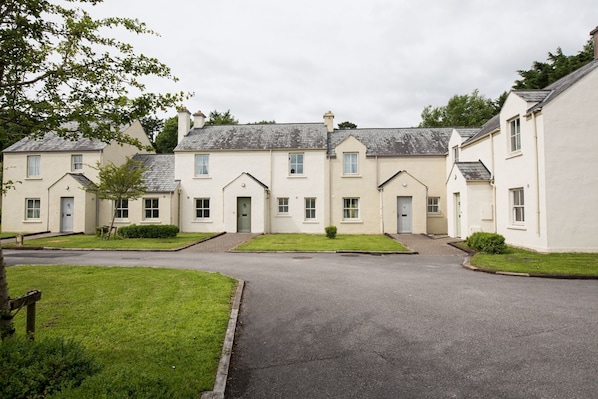 A row of two-story houses with a central driveway, surrounded by well-maintained lawns and trees. - Castle Gardens 3 bed 4018 (Bunratty)