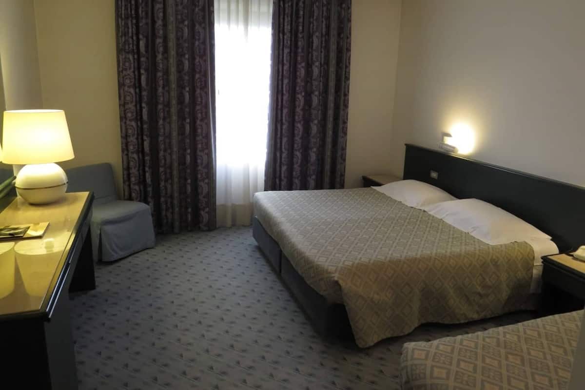 A hotel room with a bed, bedside table, lamp, curtains, and a window.