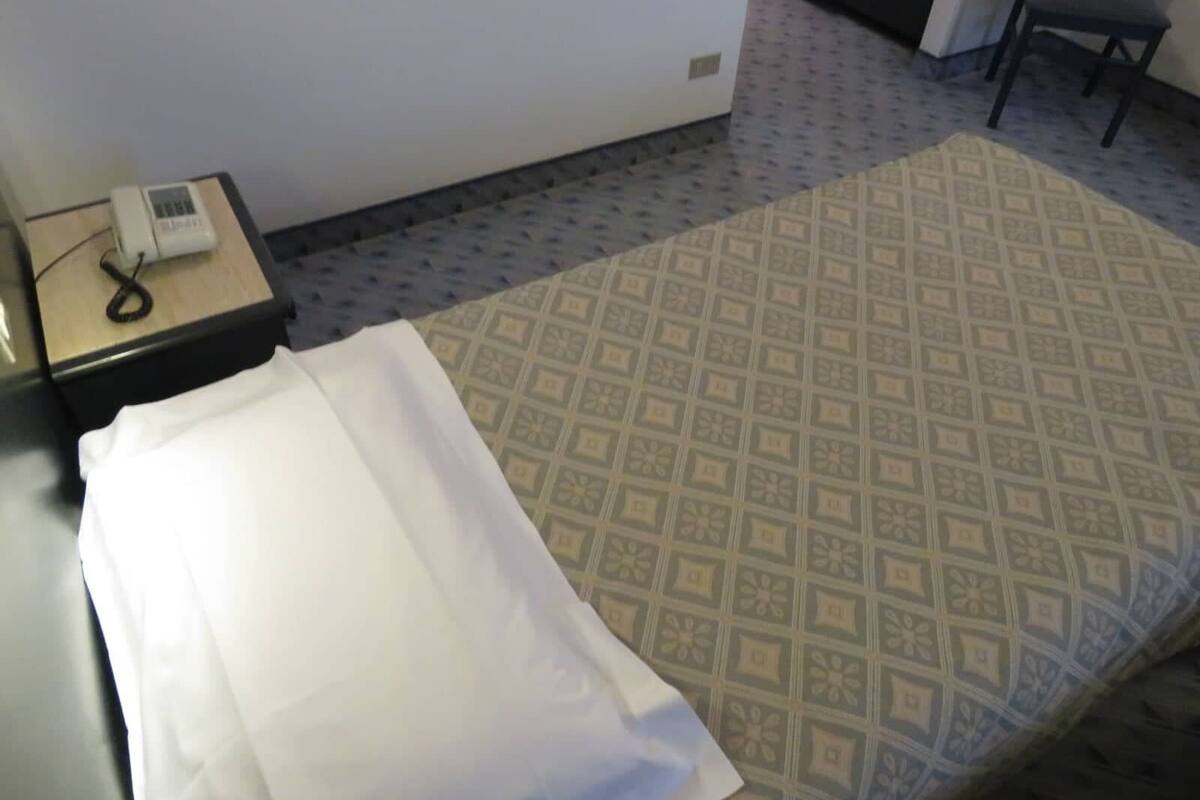 A room with a bed, a nightstand with a telephone, and a chair.