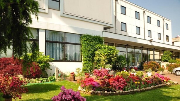 Un hotel moderno con un giardino curato, ricco di fiori e arbusti colorati.