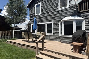 Una cabaña de troncos con terraza, mobiliario exterior y una parrilla.