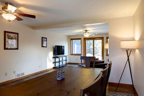 Un comedor amplio con una mesa y sillas de madera, un ventilador de techo y un televisor sobre un mueble.