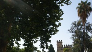 A park with a castle in the background, surrounded by trees and a paved walkway. - Hostal Alcazar I (Córdoba)