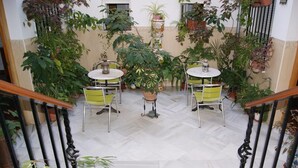 A covered patio area with two round tables and chairs, surrounded by potted plants and a tiled floor. - Hostal Alcazar I (Córdoba)
