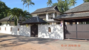 A large house with a tiled roof, a gated driveway, and palm trees in the background. - 3 Bedroom pool villa 2 SDV023-By Samui Dream Villas (Koh Samui)