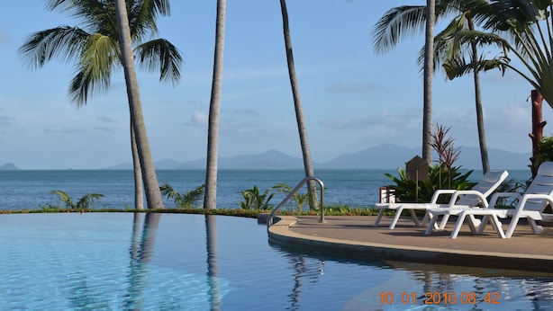 A poolside area with lounge chairs and palm trees, overlooking a body of water and distant mountains. - 3 Bedroom pool villa 2 SDV023-By Samui Dream Villas (Koh Samui)