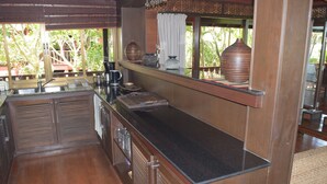 A kitchen with a black countertop, wooden cabinets, and a window with a view of greenery. - 4 bedroom beachfront Villa 3 SDV024-By Samui Dream Villas (Koh Samui)