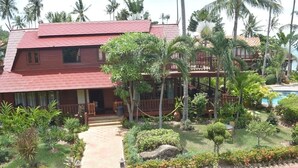 A two-story building with a red tiled roof, surrounded by lush greenery and palm trees. - 4 bedroom beachfront Villa 3 SDV024-By Samui Dream Villas (Koh Samui)
