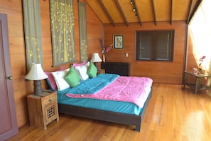 A wooden-paneled bedroom with a bed, nightstands, a window, and a wall-mounted picture.